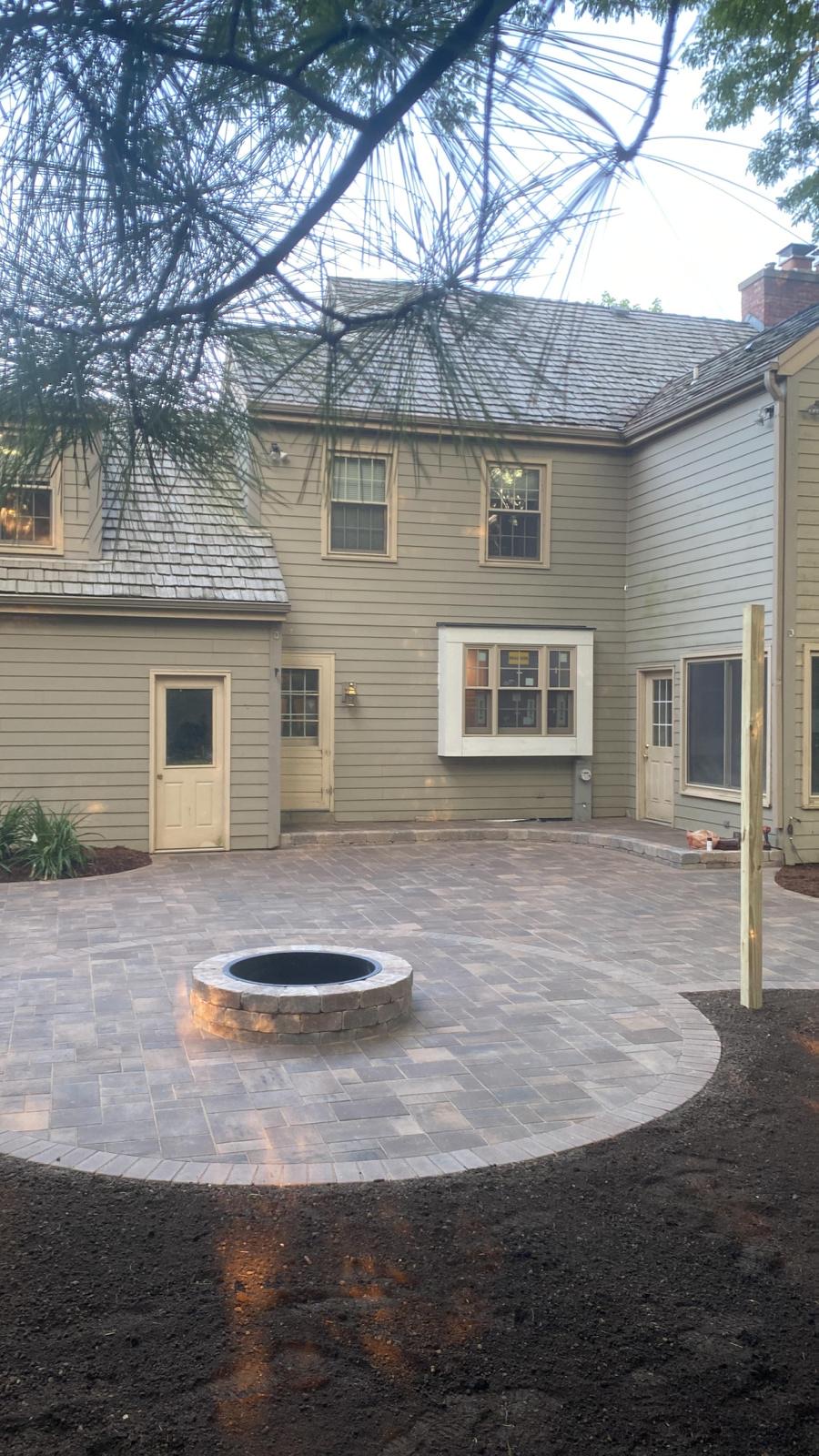 Outdoor patio with a circular fireplace in the back yard surrounded by trees.