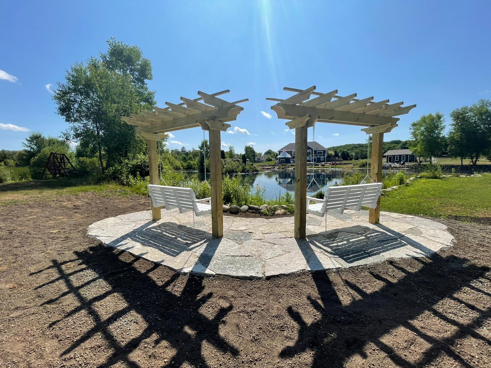 Two Pergola Bench Swings on a Flagstone Base Facing a Pond