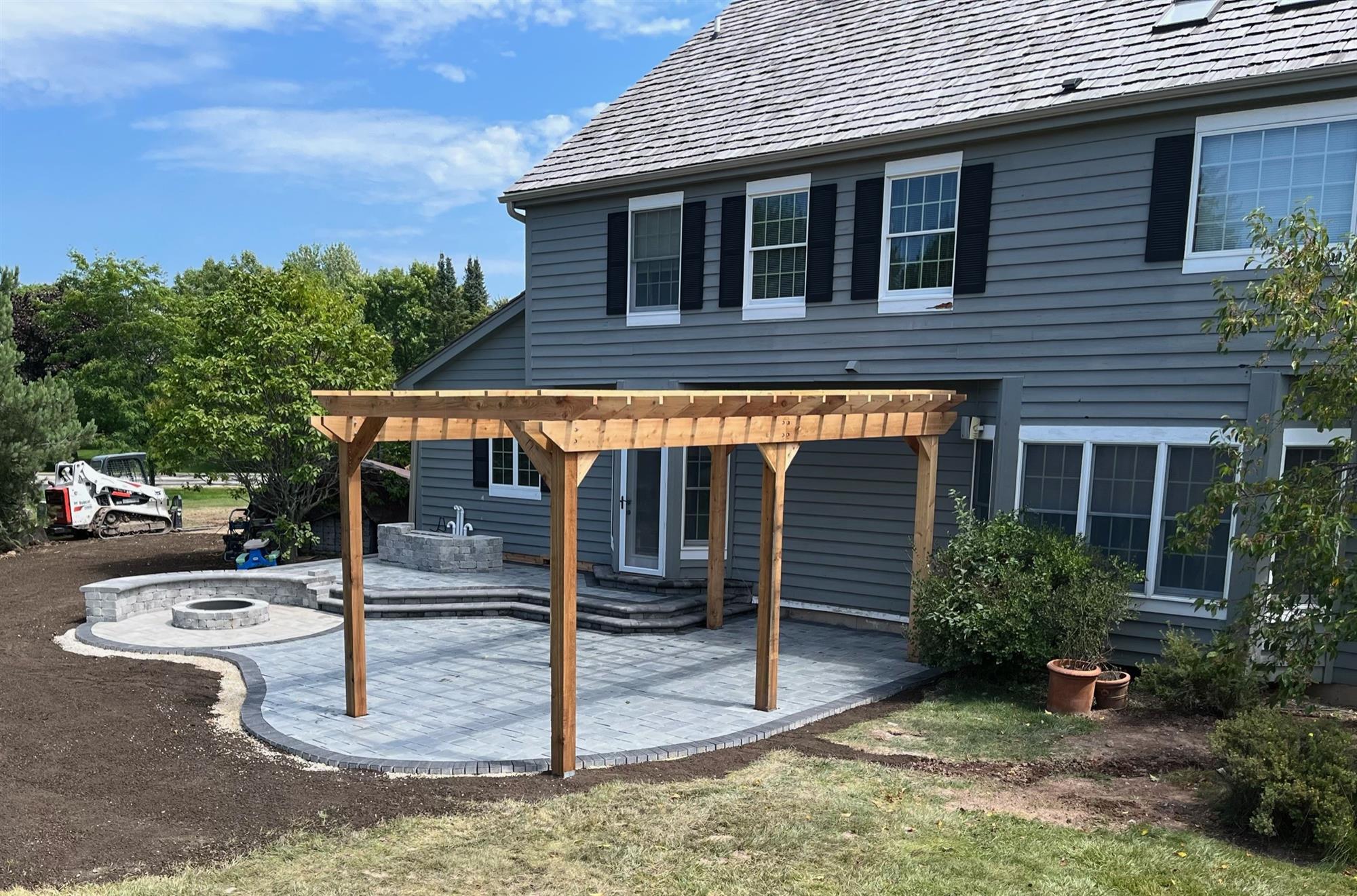 Multi-level natural stone patio with pergola, circular firepit, and landscaped surroundings.