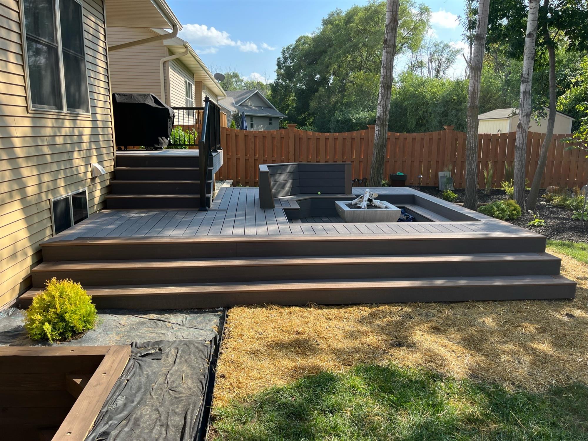 Low-Level Wood Deck with Dark Gray and Brown Tones, Small Recessed Fire Pit, Stairs from Yard, and Seating Area for Guests