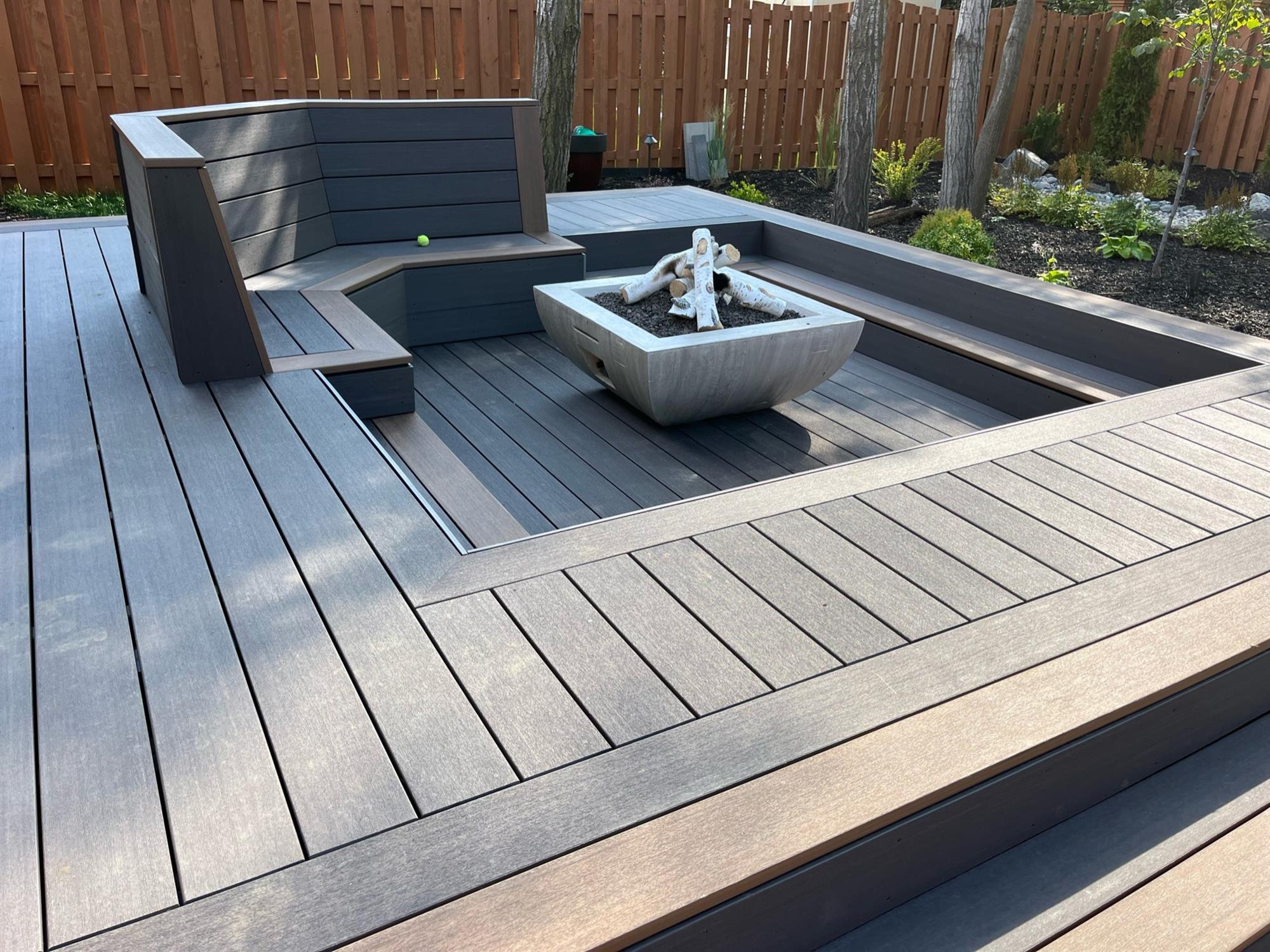 Dark grey and brown deck with built-in seating and recessed outdoor fire pit.