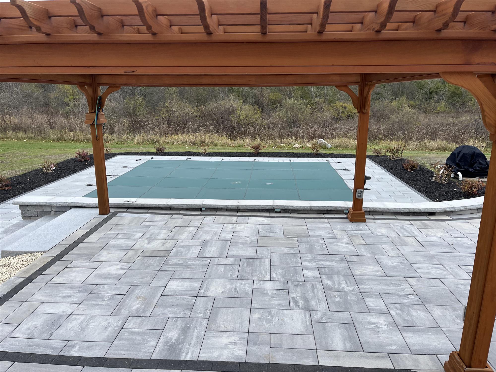 EcoPool Surrounded by a Patio with Retaining Walls and a Pergola