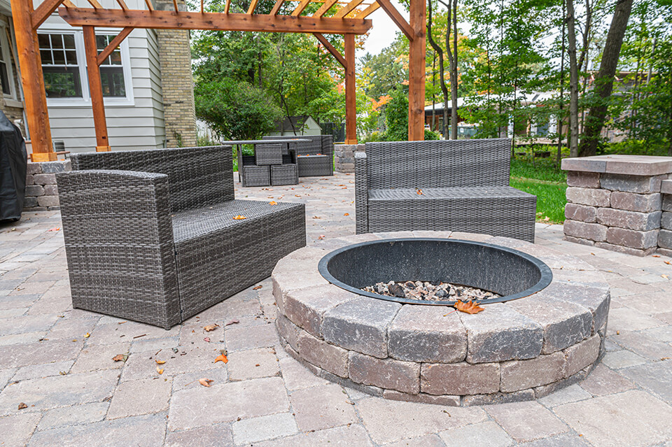 Stone paver patio with stone outdoor fire pit and wooden pergola