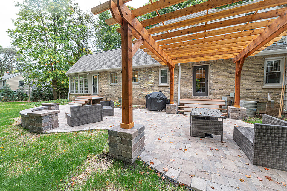 Stone patio with sitting wall & large wooden pergola attached to a house